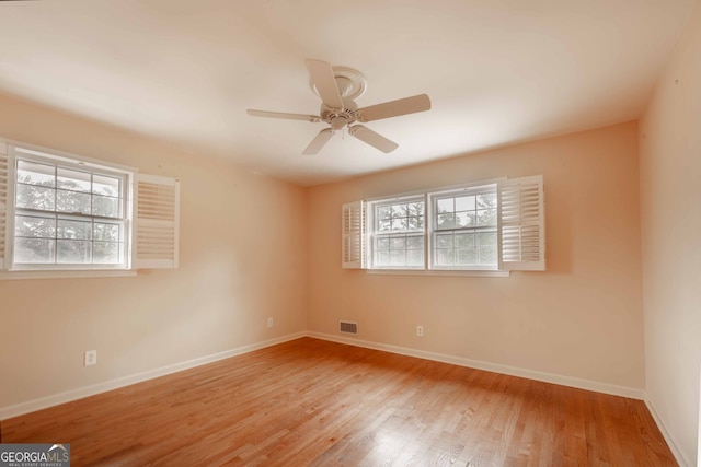 unfurnished room featuring plenty of natural light, wood finished floors, visible vents, and baseboards