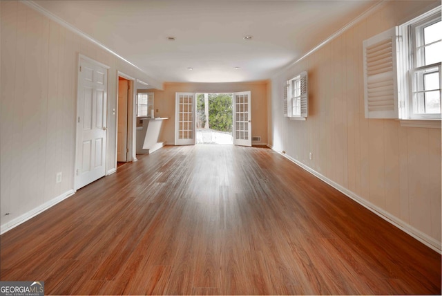 unfurnished living room with visible vents, wood finished floors, baseboards, and ornamental molding