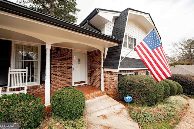 doorway to property with brick siding and roof with shingles