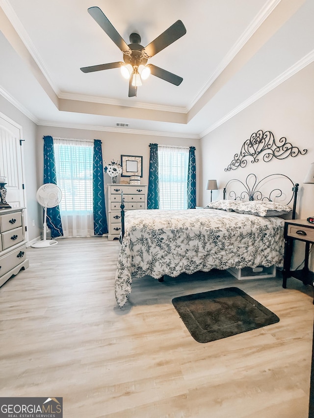 bedroom with a tray ceiling, wood finished floors, visible vents, and ornamental molding