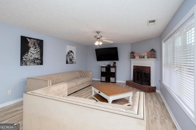 living area with a ceiling fan, baseboards, visible vents, light wood finished floors, and a fireplace