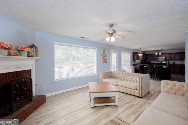 living area with visible vents, baseboards, light wood-style flooring, a fireplace, and a textured ceiling