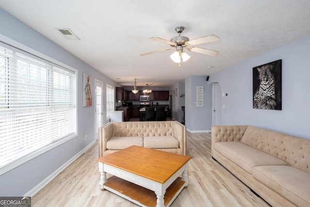 living area featuring visible vents, light wood-style flooring, a ceiling fan, arched walkways, and baseboards