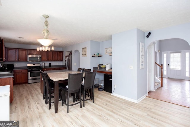 dining area with light wood-type flooring, arched walkways, and baseboards