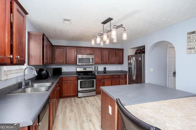 kitchen featuring light wood-style flooring, arched walkways, a sink, stainless steel appliances, and a textured ceiling