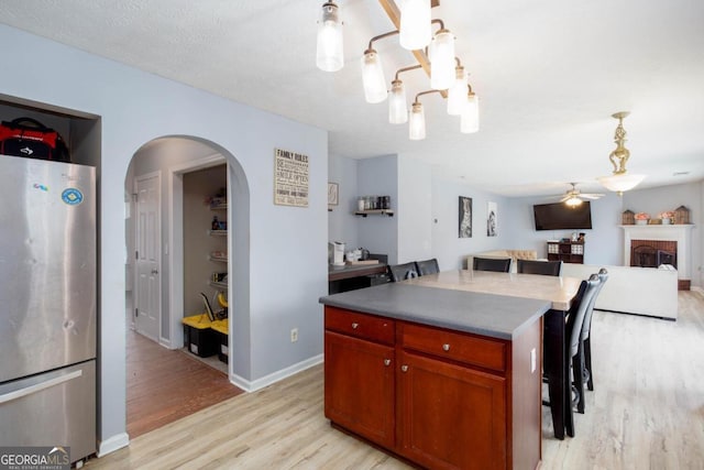 kitchen featuring open floor plan, a breakfast bar area, light wood-style flooring, freestanding refrigerator, and arched walkways