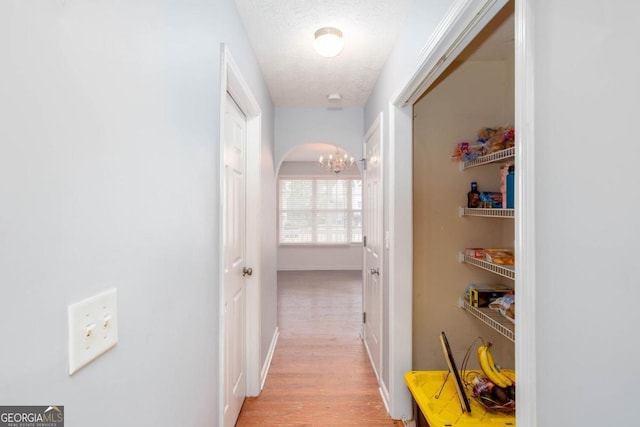 hall featuring baseboards, light wood-style flooring, arched walkways, a textured ceiling, and a chandelier