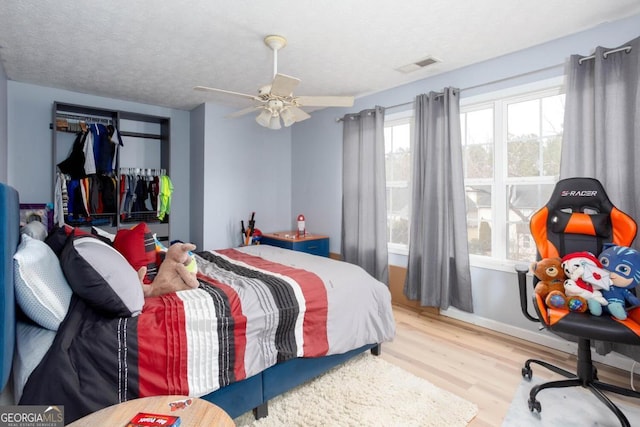 bedroom featuring a ceiling fan, wood finished floors, visible vents, and a textured ceiling