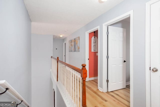 hall with an upstairs landing, baseboards, and light wood finished floors