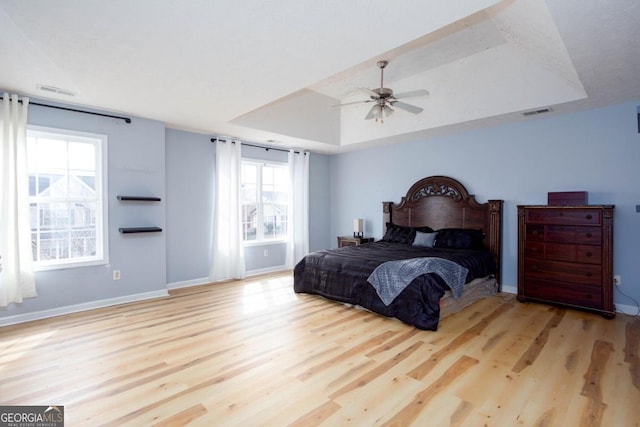 bedroom with visible vents, a raised ceiling, wood finished floors, baseboards, and ceiling fan