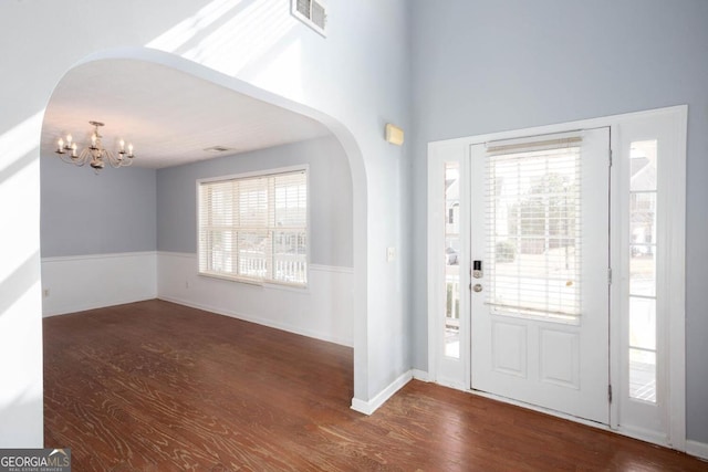 foyer entrance with arched walkways, visible vents, an inviting chandelier, and wood finished floors