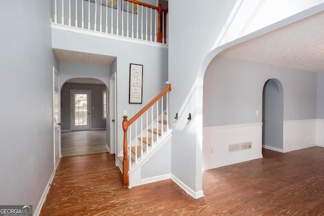 interior space with visible vents, stairs, a towering ceiling, wood finished floors, and arched walkways