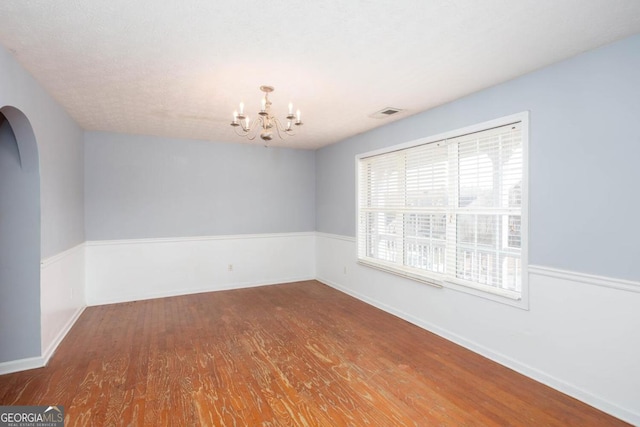 spare room with visible vents, baseboards, a chandelier, wood finished floors, and arched walkways