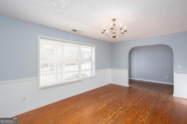 unfurnished room featuring wood finished floors, visible vents, arched walkways, a textured ceiling, and a notable chandelier