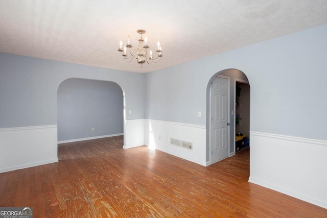 unfurnished room with arched walkways, a notable chandelier, wood finished floors, and a textured ceiling