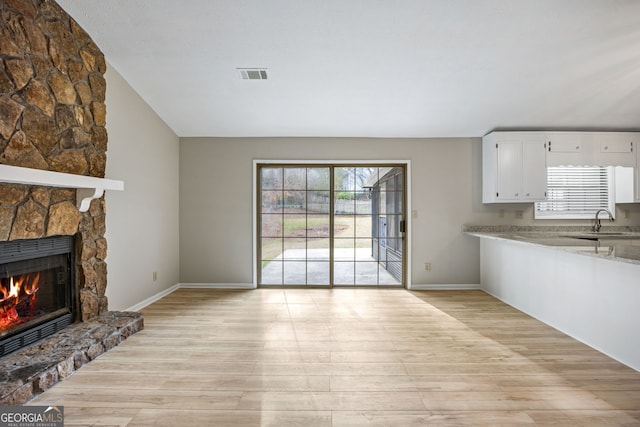 unfurnished living room featuring baseboards, visible vents, a sink, a stone fireplace, and light wood-type flooring