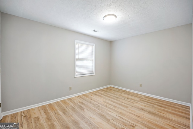 unfurnished room featuring visible vents, a textured ceiling, baseboards, and wood finished floors