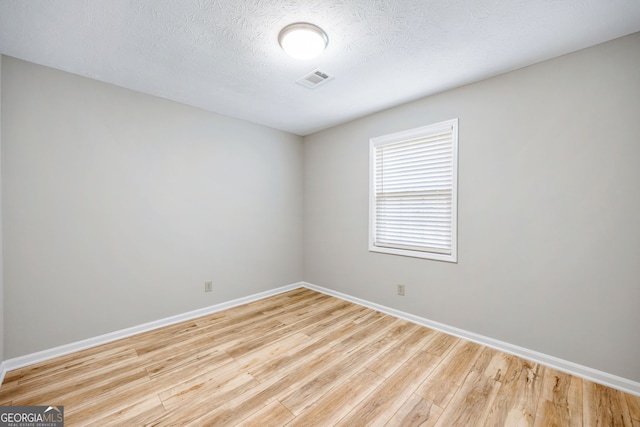 empty room with visible vents, a textured ceiling, baseboards, and wood finished floors