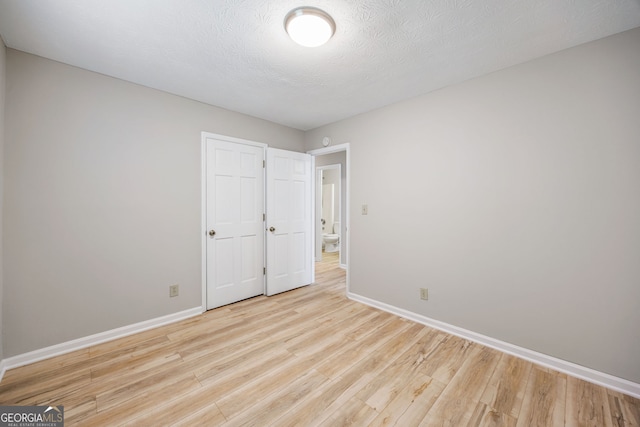 empty room with light wood-style flooring, a textured ceiling, and baseboards