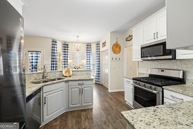 kitchen with appliances with stainless steel finishes, an inviting chandelier, a sink, dark wood finished floors, and tasteful backsplash