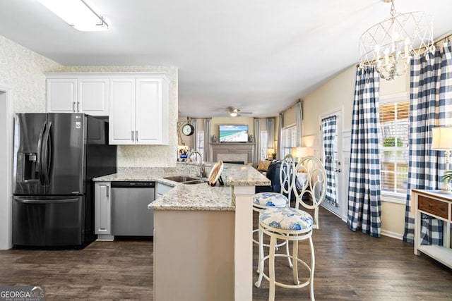 kitchen featuring appliances with stainless steel finishes, a sink, a peninsula, white cabinetry, and dark wood-type flooring