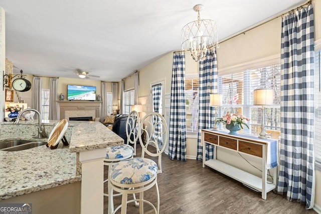 kitchen featuring light stone countertops, a sink, a fireplace, ceiling fan with notable chandelier, and wood finished floors