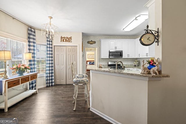 kitchen with white cabinets, light stone countertops, an inviting chandelier, stainless steel appliances, and dark wood-type flooring