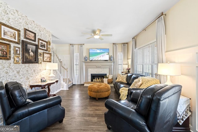 living area with a stone fireplace, a ceiling fan, dark wood-style floors, and stairway