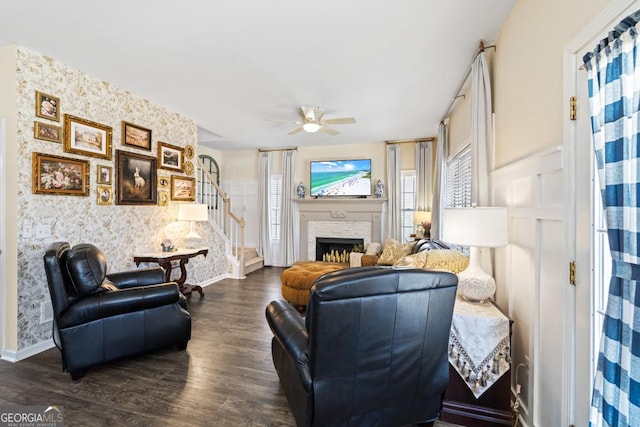 living area featuring a ceiling fan, dark wood finished floors, stairs, baseboards, and wallpapered walls