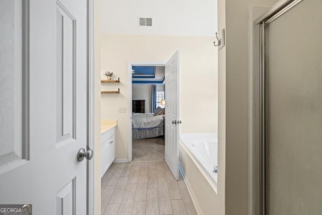 ensuite bathroom with connected bathroom, vanity, wood finished floors, visible vents, and a bath