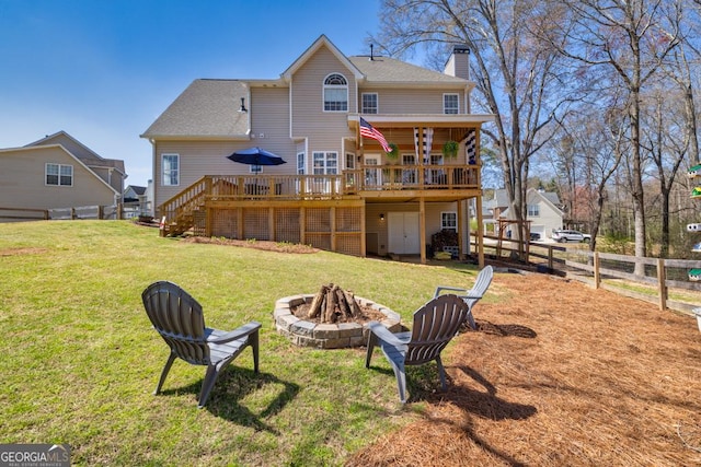 rear view of property featuring a fire pit, a wooden deck, fence, a chimney, and a yard