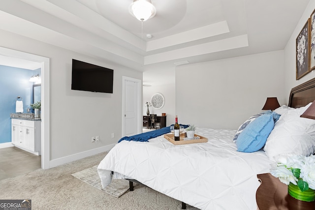 carpeted bedroom with connected bathroom, a raised ceiling, and baseboards