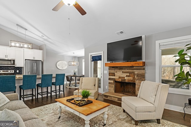 living area featuring visible vents, vaulted ceiling, a fireplace, dark wood-style floors, and a ceiling fan