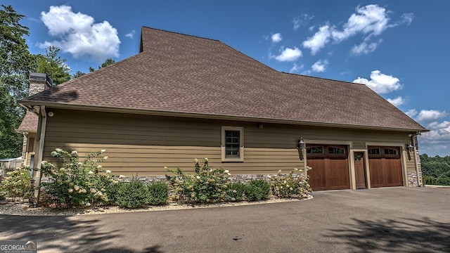 view of home's exterior featuring stone siding, a chimney, a garage, and a shingled roof