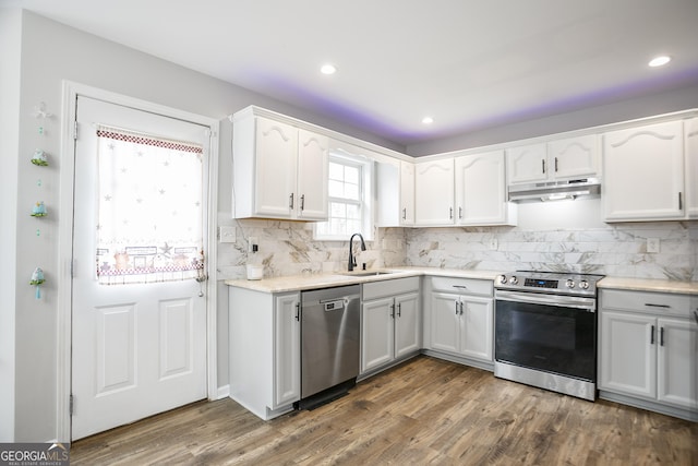 kitchen featuring a sink, under cabinet range hood, appliances with stainless steel finishes, white cabinetry, and tasteful backsplash