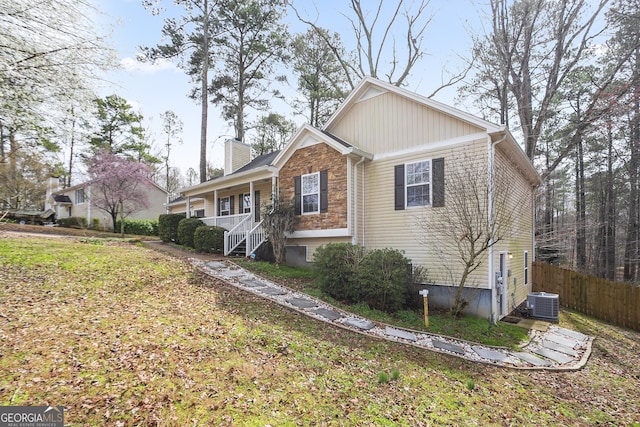 view of front of home with cooling unit, covered porch, a chimney, and fence