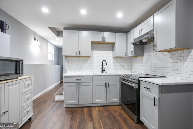 kitchen with a sink, under cabinet range hood, dark wood finished floors, recessed lighting, and appliances with stainless steel finishes