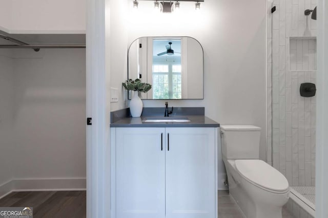 bathroom featuring baseboards, toilet, tiled shower, wood finished floors, and vanity