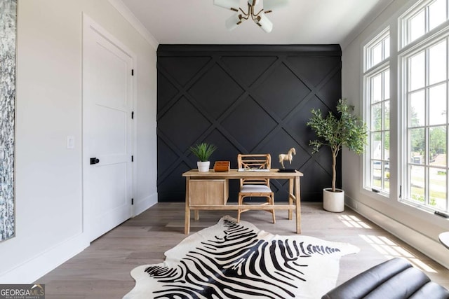 office area featuring a notable chandelier, ornamental molding, wood finished floors, a decorative wall, and an accent wall