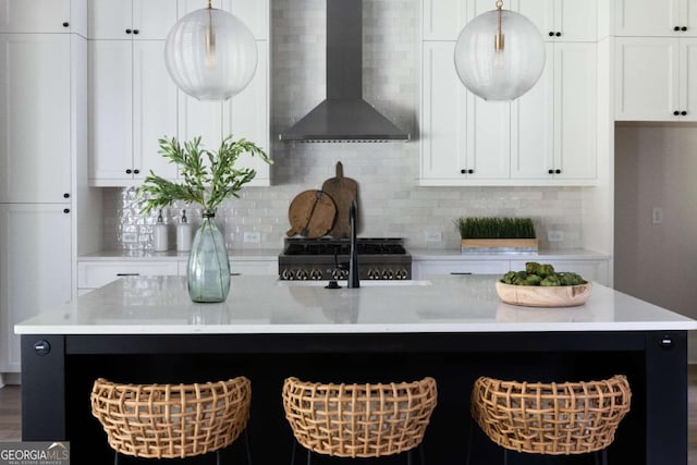 kitchen with light countertops, wall chimney exhaust hood, an island with sink, and backsplash