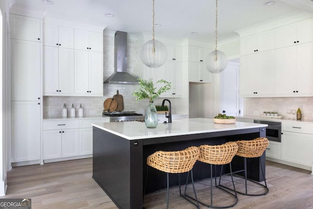 kitchen featuring a kitchen island with sink, light wood-style floors, wall chimney exhaust hood, and light countertops