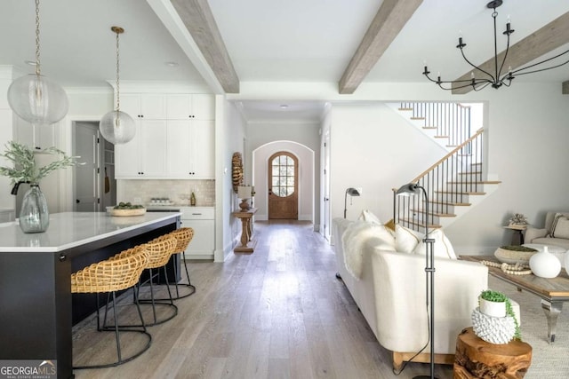 living room featuring stairway, arched walkways, crown molding, beamed ceiling, and light wood-type flooring