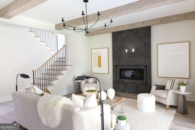 living area with beamed ceiling, stairway, a large fireplace, and wood finished floors