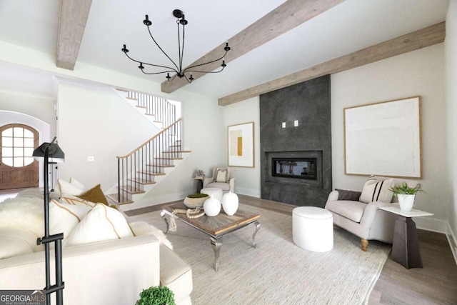 living area with wood finished floors, baseboards, stairs, beamed ceiling, and a large fireplace