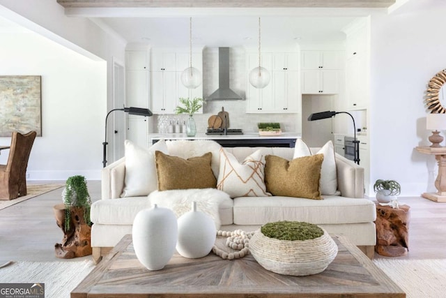 living room featuring beam ceiling, baseboards, and light wood-style floors