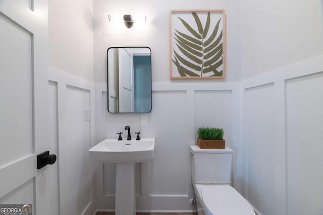 half bathroom featuring toilet, wainscoting, and a decorative wall