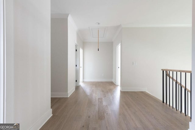 empty room with attic access, light wood-style floors, baseboards, and ornamental molding