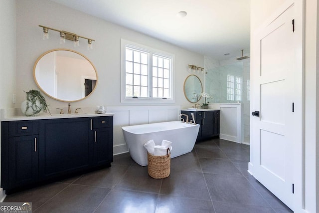 bathroom with walk in shower, two vanities, a freestanding tub, tile patterned floors, and a sink