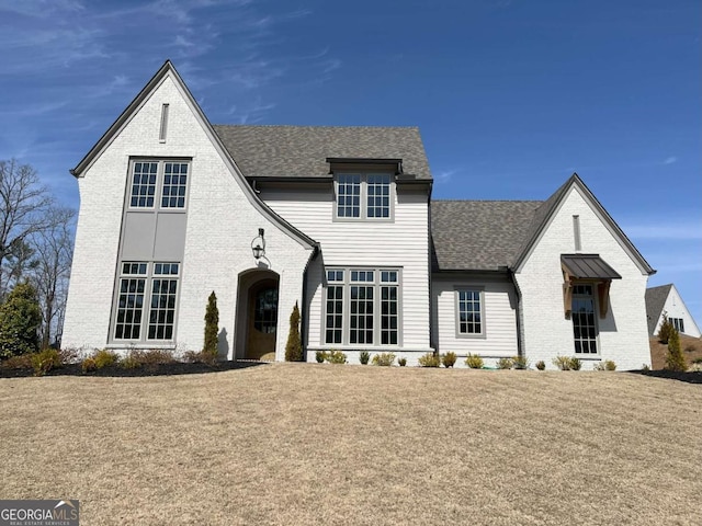 view of front of property featuring a front yard, brick siding, and roof with shingles