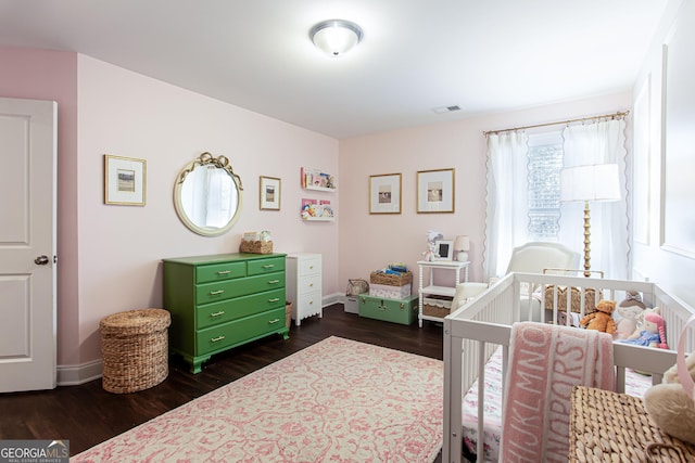 bedroom featuring dark wood finished floors, visible vents, baseboards, and a nursery area